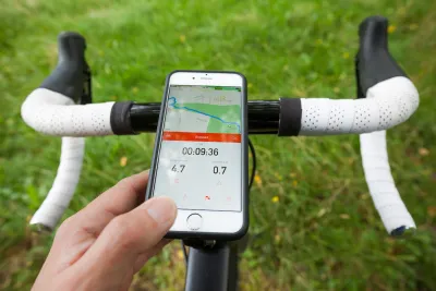 Close-up of bike handlebars with smart phone showing Strava app in handlebar holder. Green grass in background.