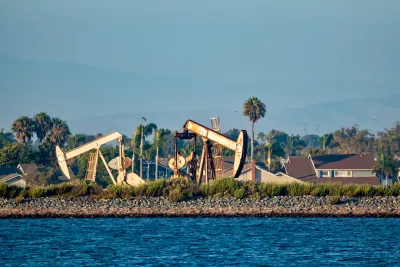 Oil drilling pumps on a wetland beach in California with houses in background