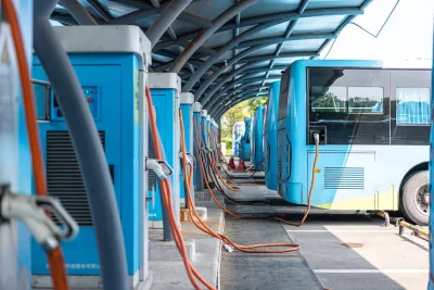 Row of blue electric buses parked and plugged in at charging station.