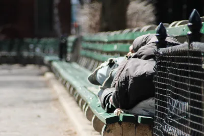 Person in black hoodie sleeping on green park bench in New York City park