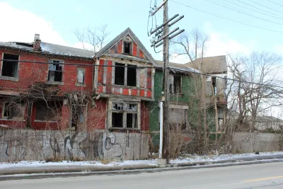 Vacant two-story red brick home in Detroit with missing windows.
