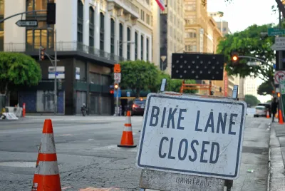 Close-up of Bike Lane Closed sign on street in downtown Los Angeles with orange traffic cones blocking lane in background.