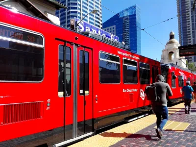Red San Diego Trolley light rail train at station with passengers walking on platform and Spanish-style dome building in background.