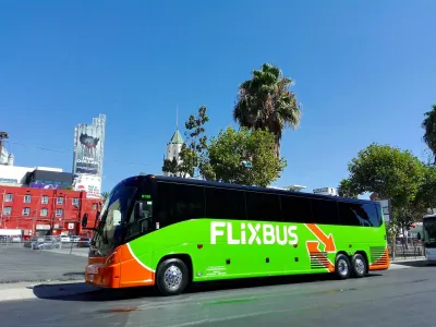 Green Flixbus bus parked on street in Los Angeles, California with palm trees and Hollywood buildings in background on sunny day.