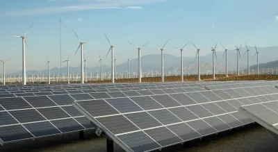 Large solar panel installation and wind turbines with Southern California desert mountains in background.