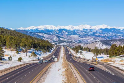 View of Colorado highway with light traffic and snowy Rocky Mountains in background.