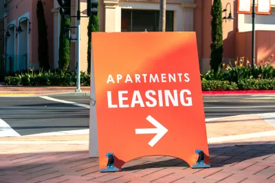 Orange "Apartments Leasing" sandwich board sign on sidewalk with arrow pointing right.