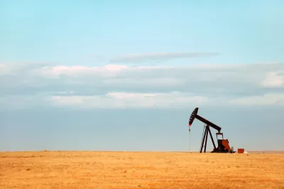 Single oil derrick on dry prairie with faded blue sky in background.