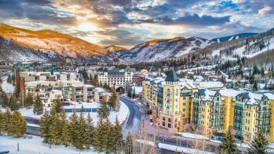 Aerial view of Vail, Colorado ski resort town with multi-story buildings in foreground and snowy mountains in background.