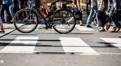 Low shot of pedestrians and a bike crossing a striped crosswalk.