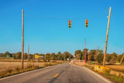 Two-lane rural road with stoplights hanging above roadway and construction visible in distance.