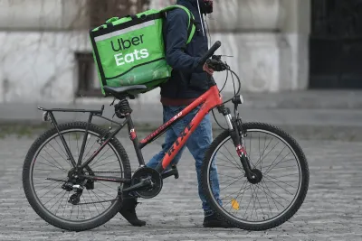 Person walking red bicycle with green Uber Eats delivery bag on cobblestone street in Bucharest, Romania.