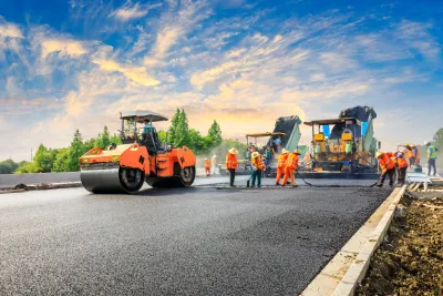 Crew in orange safety vests stand on roadway next to orange heavy equipment
