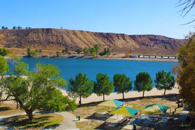 A view of a recreational area in front of a bright blue Castaic Lake in LA County with arid flat hills in the background.