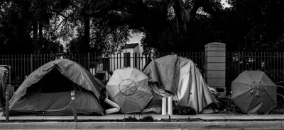 Black and white photo of row of tents set up against fence outdoors.