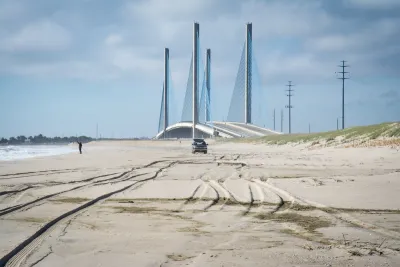 View of sand dunes with one truck and one fisherman at seashore in Delaware with Indian River Inlet Bridge in background.