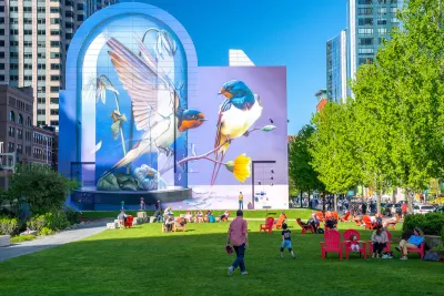 People enjoying a sunny day on a green lawn with pink lawn chairs and colorful bird mural in background in Boston, Massachusetts.
