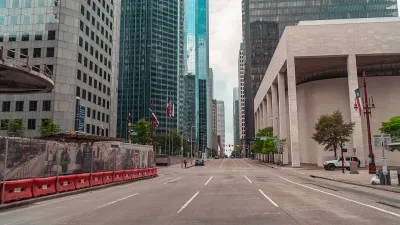 Large brutalist building and skyscrapers viewed from middle of wide street in downtown Houston, Texas.