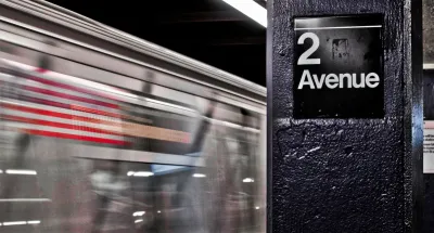 Close-up of 2 Avenue sign on column in NYC subway station with train passing by in background.