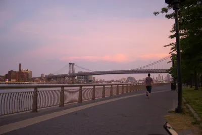 Sunset view of Williamsburg Bridge from East River Park walkway next to river with one jogger.