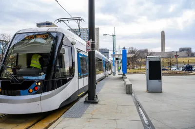 White and blue Kansas City streetcar at a station with LIberty Memorial column in background.