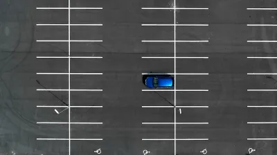 Bird's eye view of empty asphalt parking lot with one blue car.
