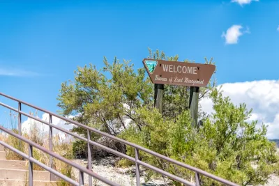 Wood WELCOME sign with Bureau of Land Management name and logo next to concrete stairwell outdoors in Utah.