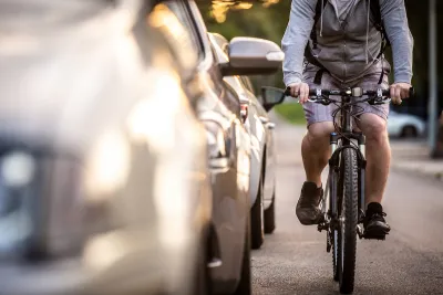 Man on bike rides next to parked cars.