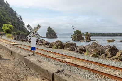 Railroad crossing sign next to tracks along rocky coast in Oregon.