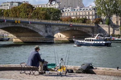 Man sitting in chair along River Seine in Paris with fishing pole.