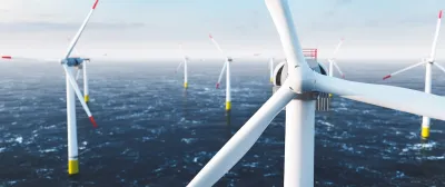 Close-up of top of white offshore wind turbine with other turbines in sea in background.