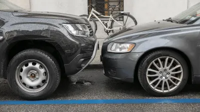 Two grey cars parked nose to nose, one taller than the other, on city curb with parked bicycle visible on sidewalk.