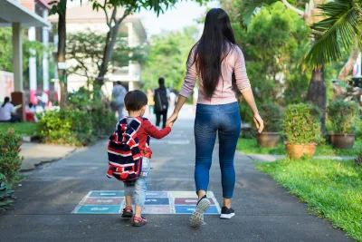 View from back of mother and hcild holding hands and walking down asphalt walkway painted with game grid.