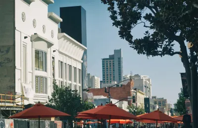 The tops of umbrellas for outdoor dining spaces are visible with large buildings in the background on a sunny day in the city of San Diego.