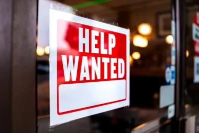 Close-up of Help Wanted sign with white text on red background posted inside storefront window.