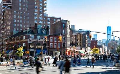 Street scene in Greenwich Village, New York City with people walking through busy intersection and new WTC tower in background.