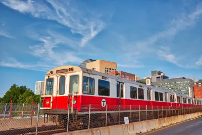 Red T train passing on elevated rail with Boston buildings in background.