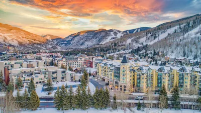 Aerial view of Vail, Colorado in winter with multi-story buildings in foregorund and snowy mountains in background.