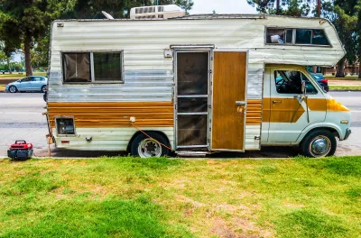 Old white motor home with brown stripe and open door parked on street in Los Angeles, California.