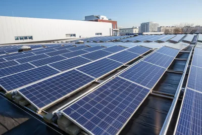 Rows of solar panels on a large rooftop with office or industrial buildings in background.
