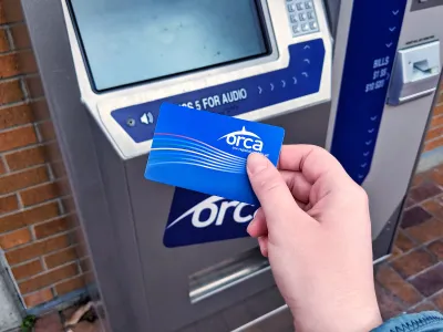 Close-up of person's hand holding blue ORCA transit fare payment card in front of fare payment machine.