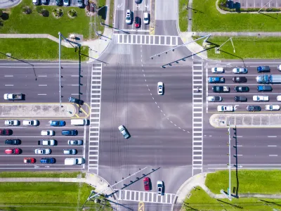 Bird-s eye view of multi-lane road intersection with medians and crosswalks.