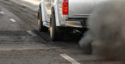 Close-up of driver's side of silver truck with cloud of dirty emissions from tailpipe.
