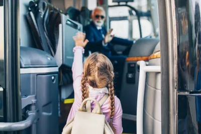Young girl with pigtail braids boarding bus with blurred bus driver in driver's seat in background