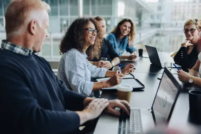 Men and women having a business meeting around a conference table in a glass-walled office building
