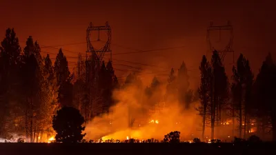 Wildfire burning under power transmission towers and large trees at night.