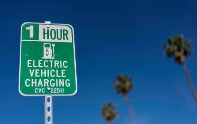 Close-up of green and white sign for 1 hour EV charging station outdoors with tall palm trees in background against blue sky.