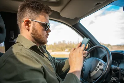 Man sitting in driver's seat looking at cell phone.