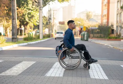 Young man in wheelchair crossing zebra crosswalk.