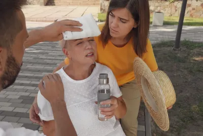 Two people helping an older woman outdoors suffering from heat stroke.